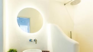 Ein Badezimmer mit rundem Spiegel, Waschtisch aus Holz, weißem Waschbecken und einer Dusche.