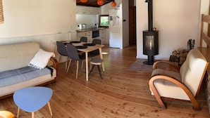 A spacious living area with a sofa, dining table, and chairs, a kitchen in the background, and a wood-burning stove.