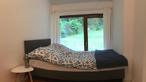 A bedroom with a bed, a small bedside table, and a window with a view of a green landscape.