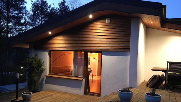 A modern house with a wooden deck, a large window, and a small outdoor seating area.