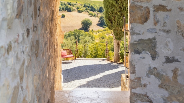 Un pasillo de piedra que lleva a un arco de madera, con vista a un paisaje verde y una silla roja.