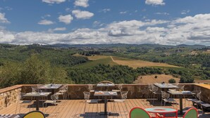 Una terraza al aire libre con mesas y sillas, con vistas a un paisaje montañoso con viñedos.