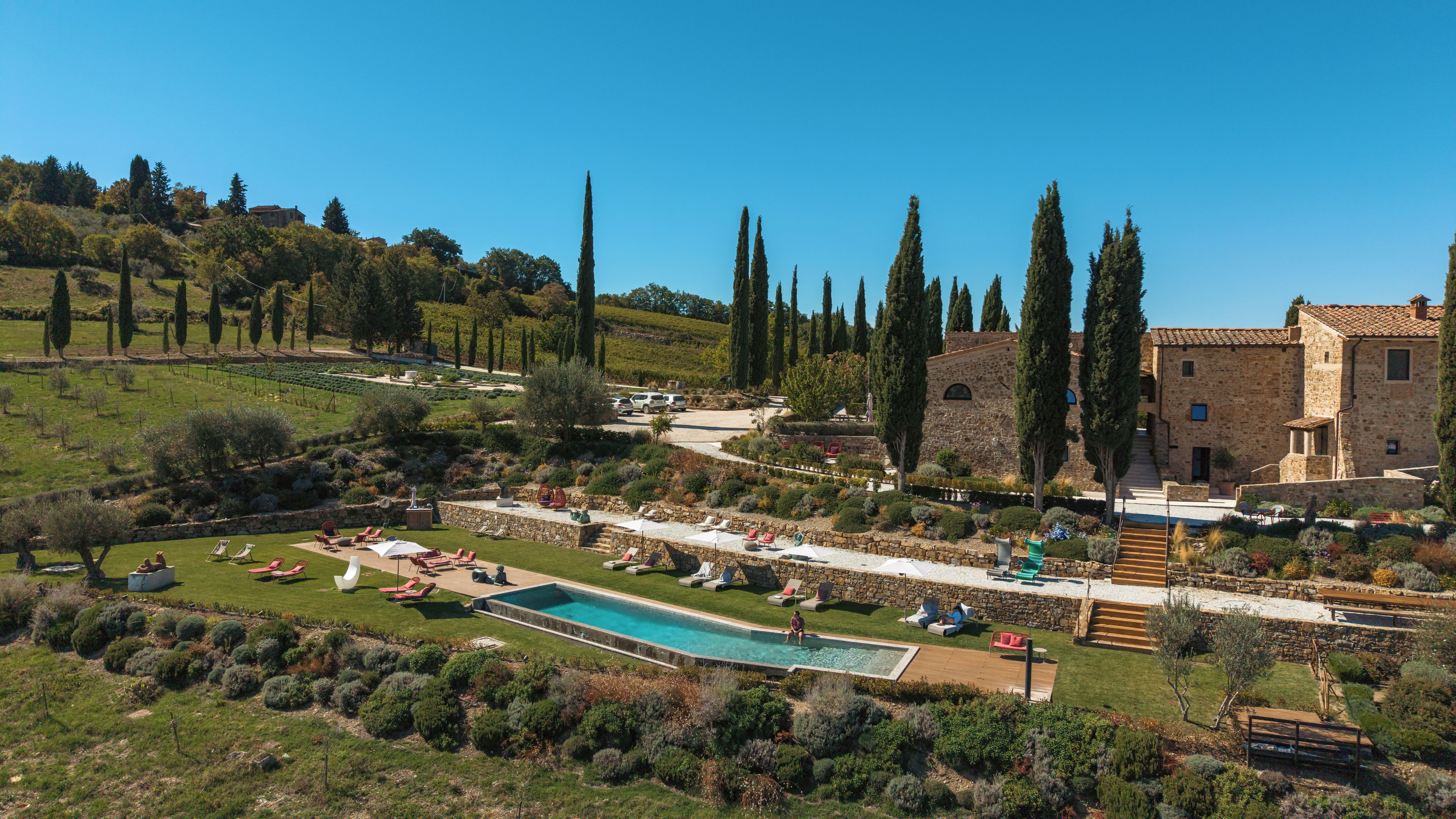 Un espace piscine avec des chaises longues, un bâtiment en pierre et un vignoble en arrière-plan.