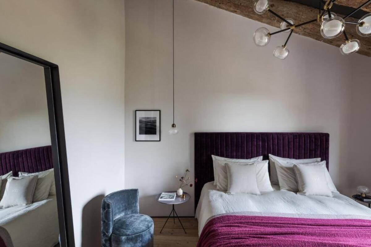 A bedroom with a large bed, a chair, a small table, and a mirror.