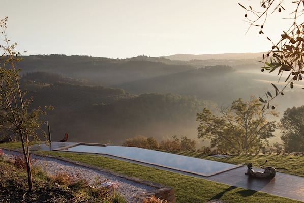 A serene landscape with a clear view of a pool, a chair, and a statue in a garden setting.