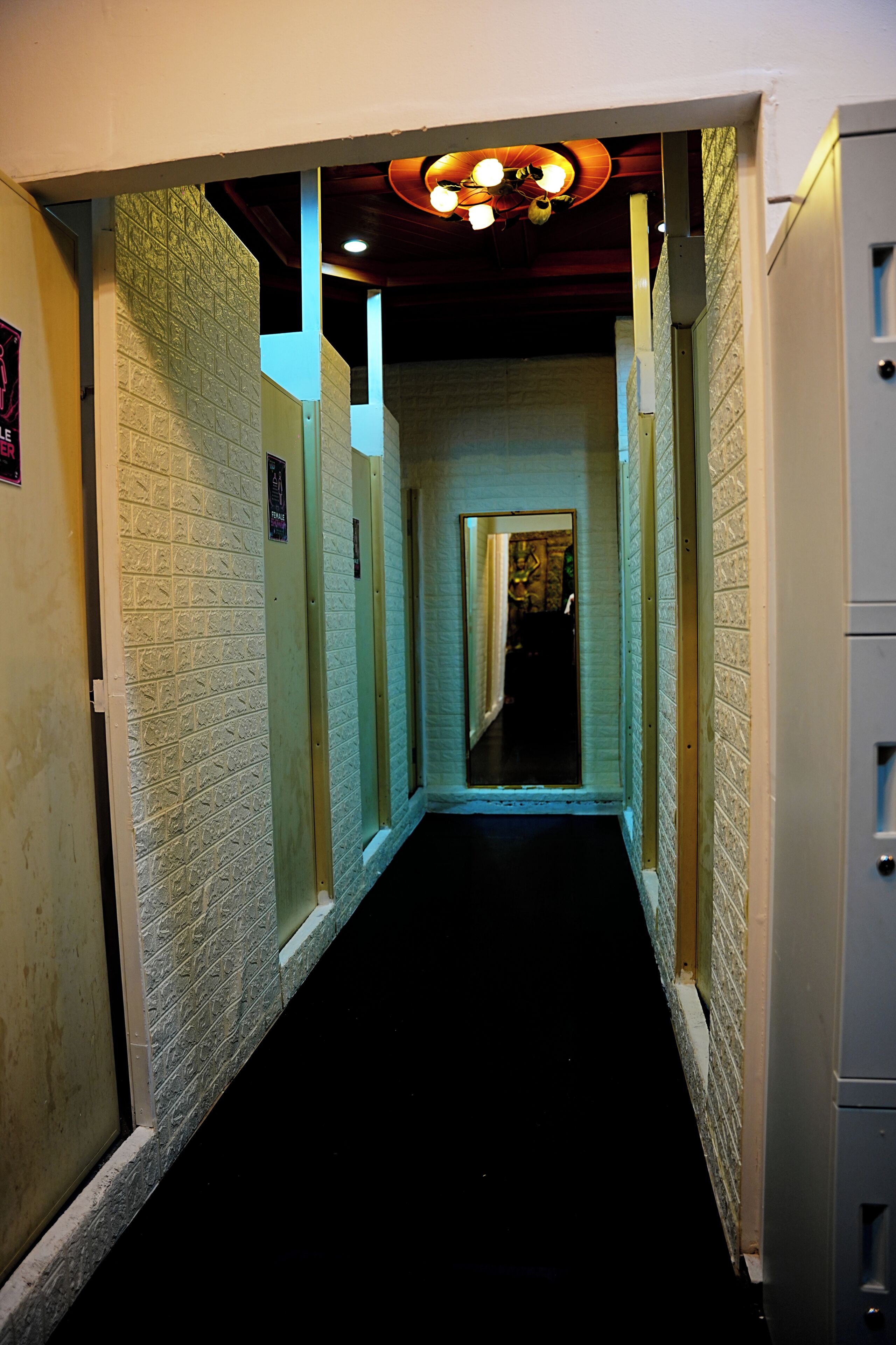 Een gang met een zwart tapijt, witte muren met structuur en een plafond met een ronde lamp.