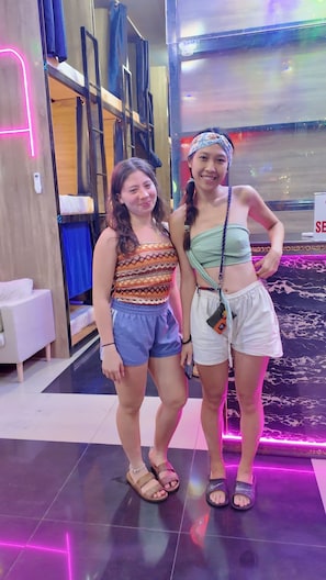 Two people standing in a room with bunk beds and a neon-lit floor.