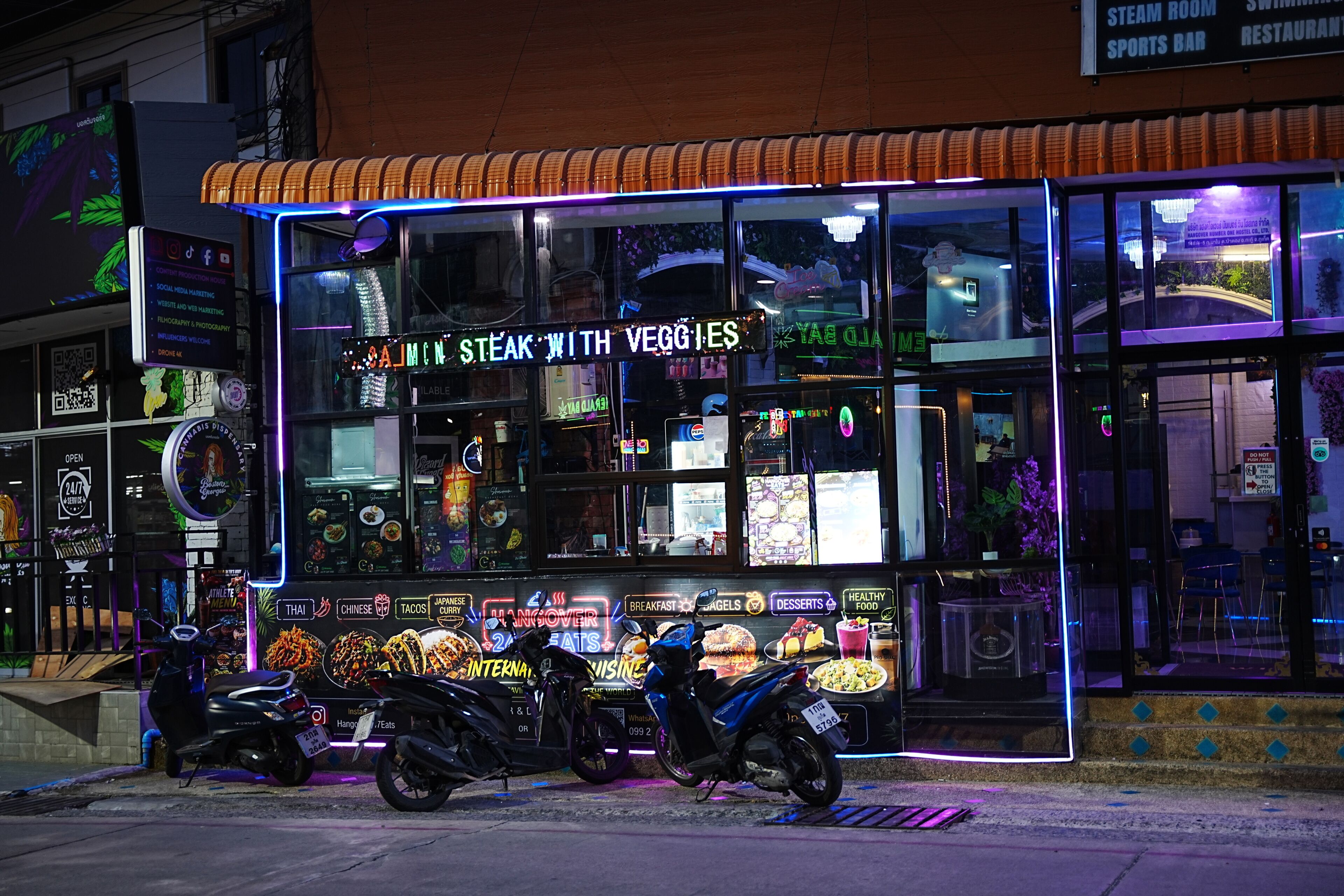 A food stall with neon signage advertising 'Steak with Veggies' and 'Hangover 2 Meals'.