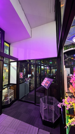 A modern building entrance with glass doors, a clear plastic structure, and a purple-lit ceiling. - Hangover Hostel Patong (Patong)