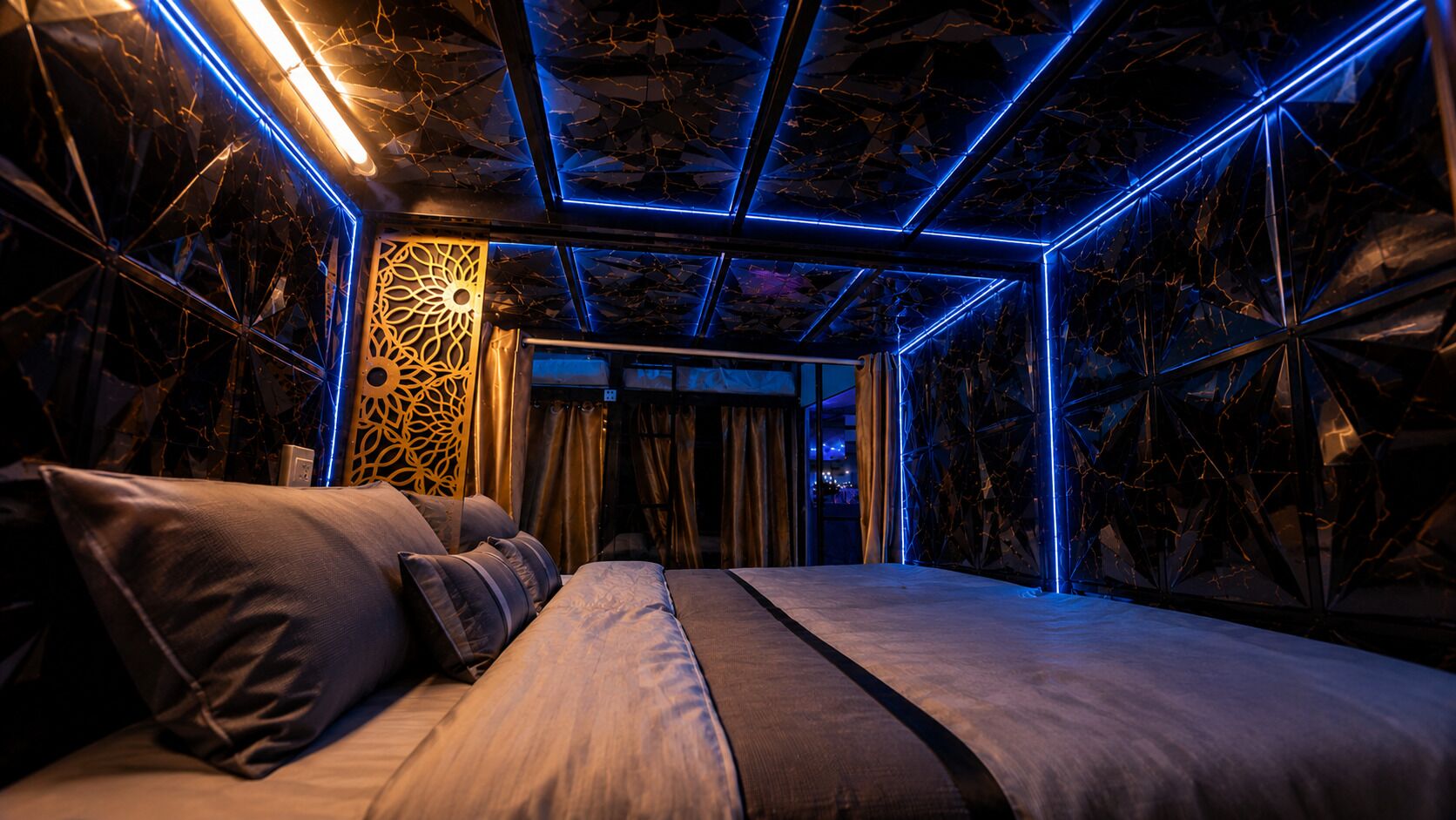 A modern room with a bed, a decorative wall panel, and a geometric ceiling design.