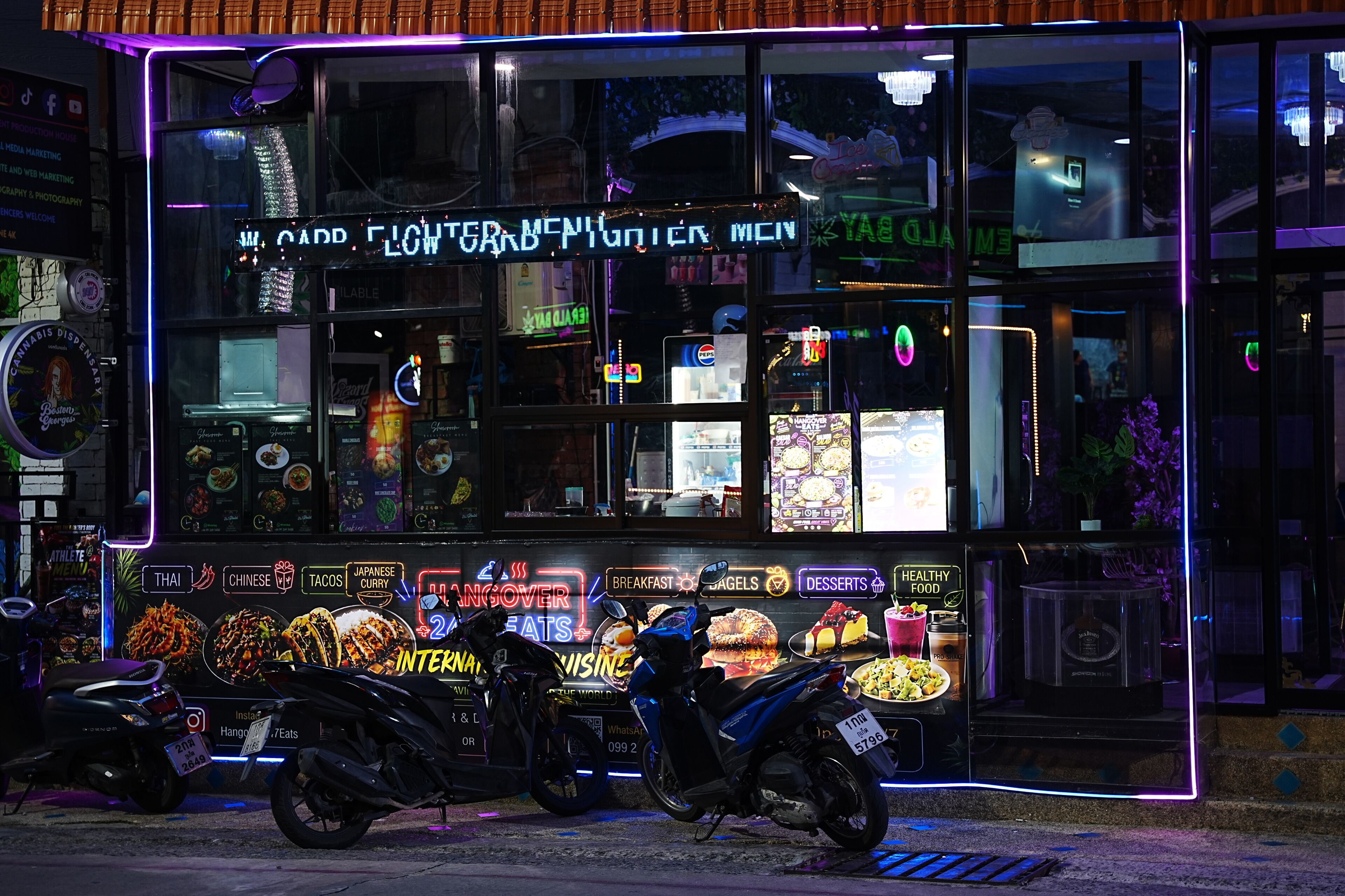 A brightly lit storefront with neon signs advertising various food options and a digital menu display.
