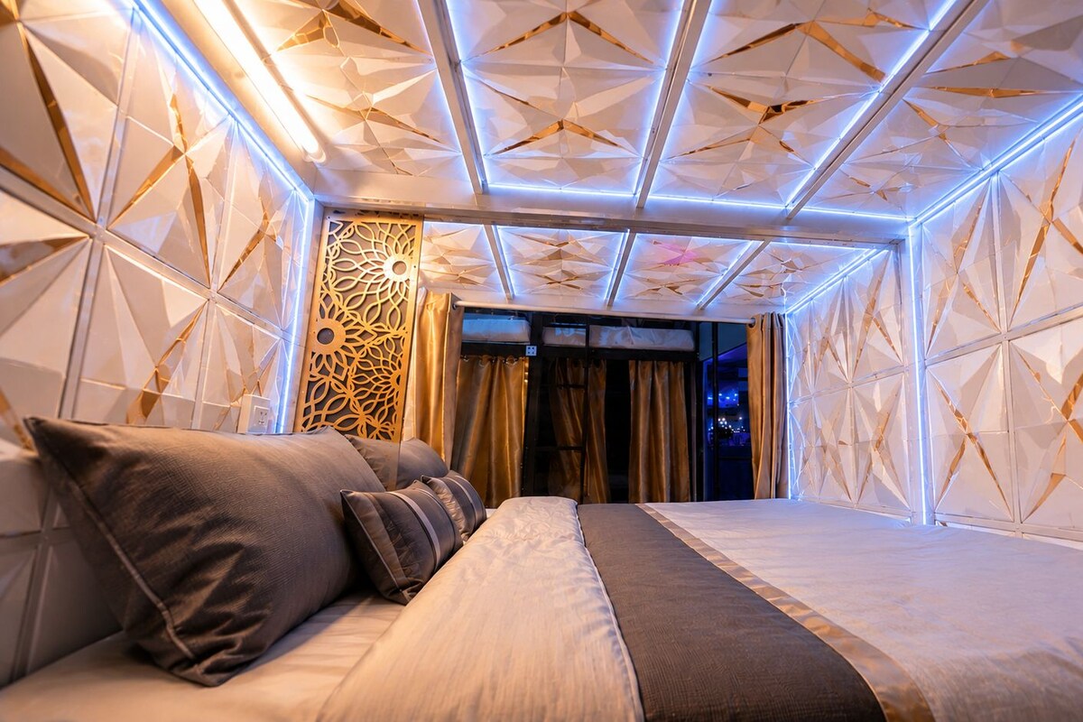 A modern hotel room with a geometric patterned ceiling, a bed with a headboard, and a decorative wall panel.