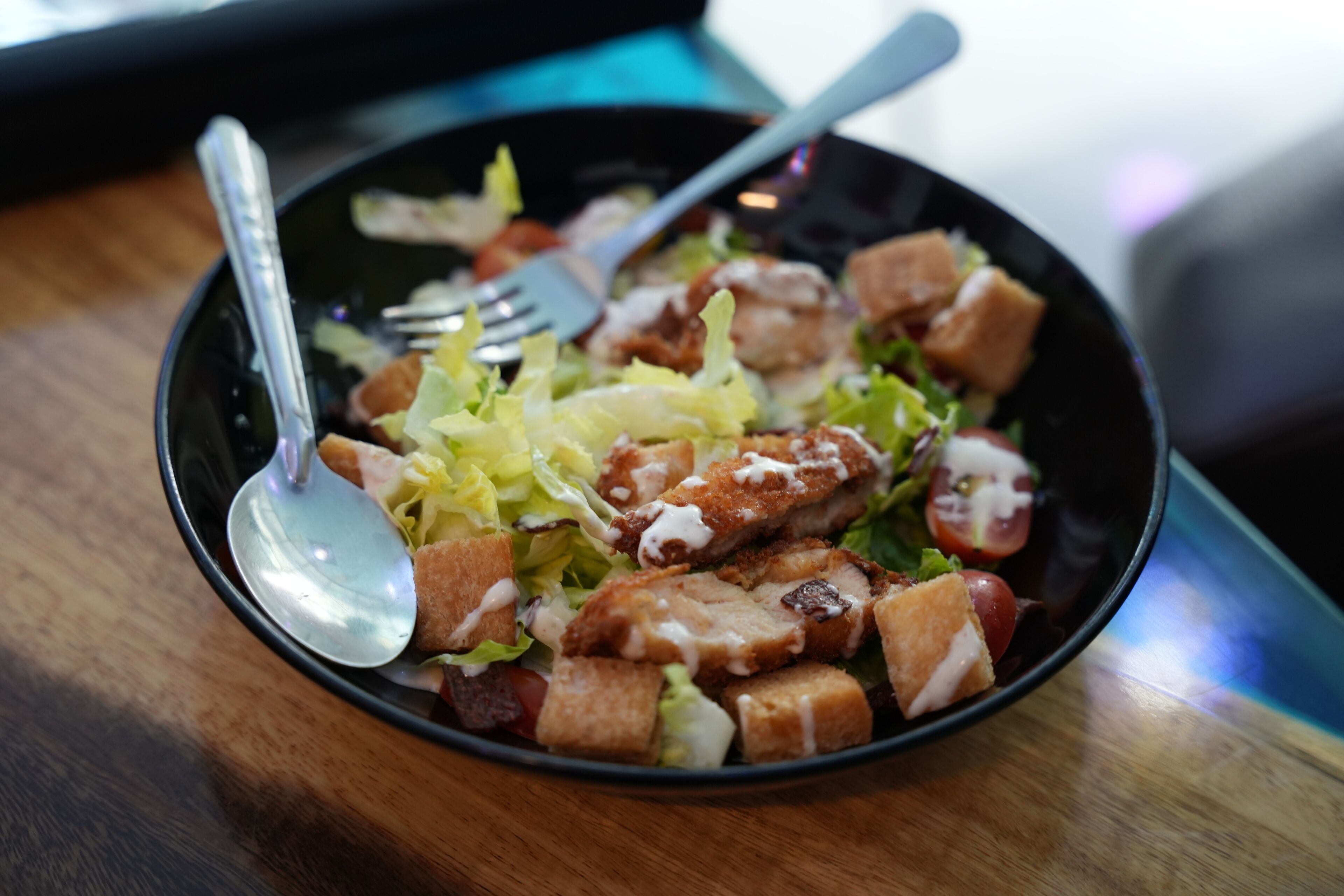 A salad with croutons and a fork on a wooden table.