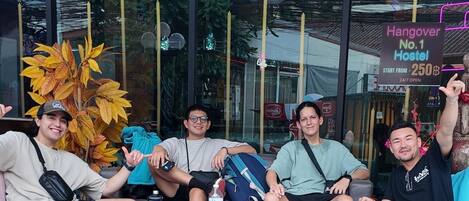 A group of people sitting on a bench outside a building with a sign advertising a hostel.