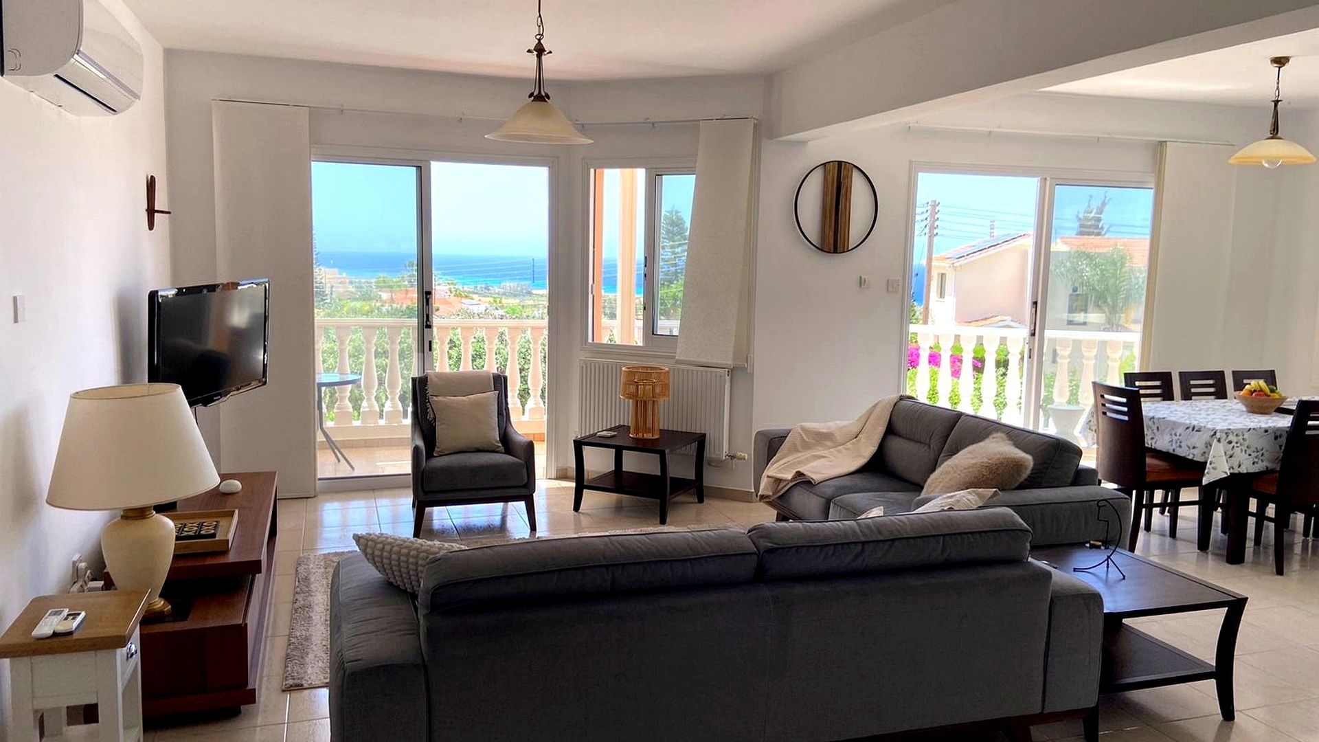 A living room with a sofa, armchairs, a TV, and a dining area with a table and chairs.