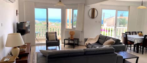 A living room with a sofa, armchairs, a TV, and a dining area with a table and chairs.