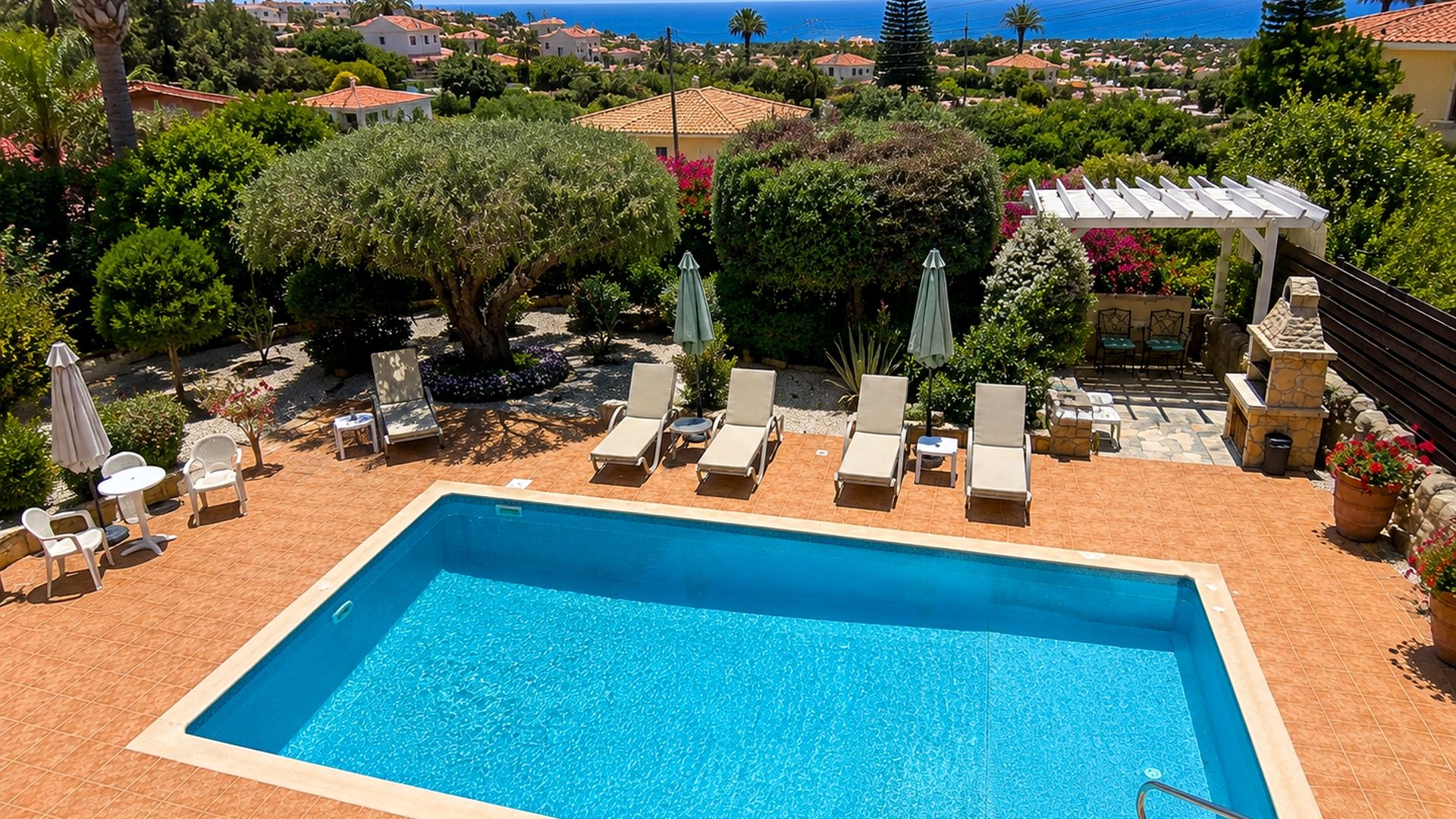 Piscina rectangular con tumbonas y sombrillas, rodeada de vegetación y vistas al mar.