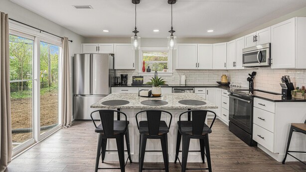 A modern kitchen with white cabinets, a central island with bar stools, stainless steel appliances, and pendant lighting. - Secluded ½-acre retreat surrounded by trees for ultimate privacy and quiet. Remodeled and beautifully furnished with modern finishes. Enjoy a peaceful setting just 8 minutes from Belton/Raymore—perfect for relaxing stays or extended work trips. (Grandview)