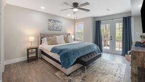 A bedroom with a bed, a nightstand, a ceiling fan, a window with curtains, and a view of the outdoors. - Secluded ½-acre retreat surrounded by trees for ultimate privacy and quiet. Remodeled and beautifully furnished with modern finishes. Enjoy a peaceful setting just 8 minutes from Belton/Raymore—perfect for relaxing stays or extended work trips. (Grandview)