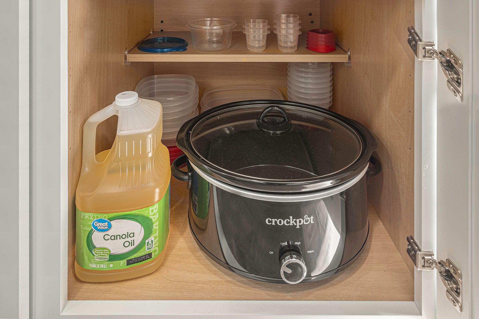 Ein Küchenschrank mit einem Slow Cooker, einem Kanolaöl-Kanister und Plastikbehältern.