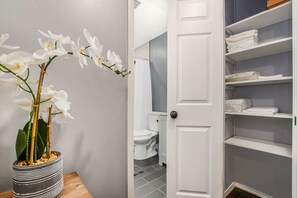 Ein Badezimmer mit Toilette, einer Dusche und einer weißen Tür zu einem Stauraum mit Regalen.