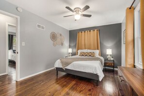 Ein Schlafzimmer mit Bett, Nachttischen, Deckenventilator und einem Fenster mit Vorhängen.