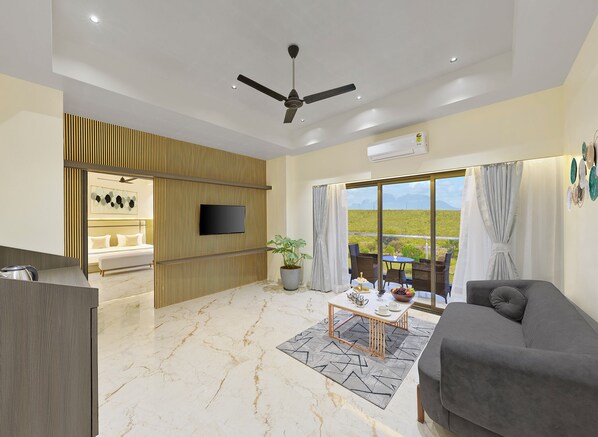 A modern living room with a sofa, a coffee table, a TV mounted on a wall, and a balcony with a view of the countryside.