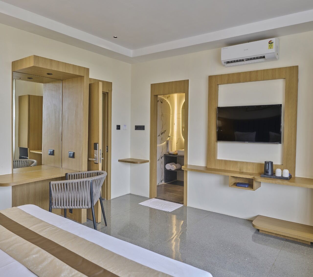 Une chambre d’hôtel moderne, dotée d’un grand lit, d’un bureau avec une chaise, d’une télévision et d’une salle de bain visible à travers une porte ouverte.