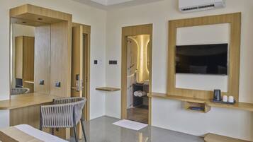 Une chambre d’hôtel moderne, dotée d’un grand lit, d’un bureau avec une chaise, d’une télévision et d’une salle de bain visible à travers une porte ouverte.
