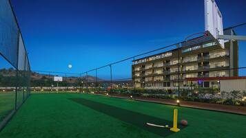 Una cancha deportiva con una red, un campo de cricket y un aro de baloncesto.