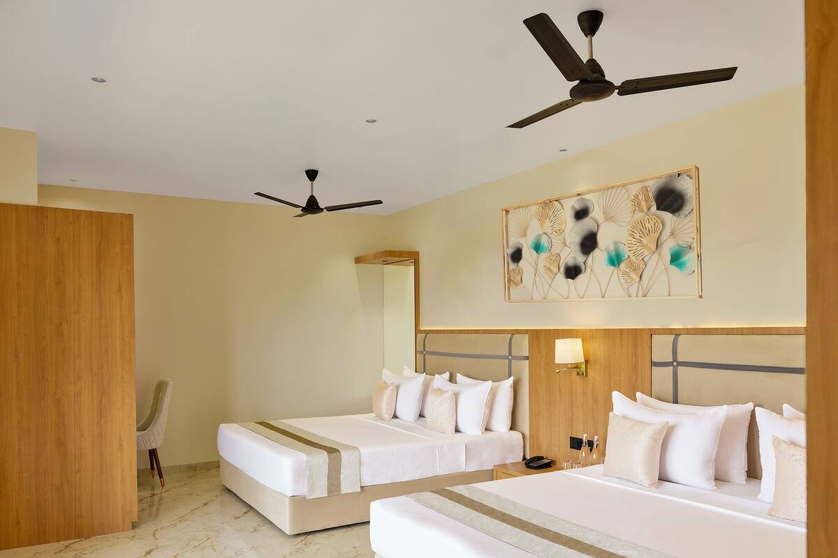 Habitación de hotel con dos camas, ventilador de techo, armario de madera, suelo de mármol y un adorno en la pared.