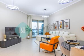 A modern living room with a sofa, a dining table, and a TV. There are two pendant lights and a large window with curtains.