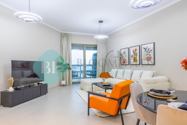 A modern living room with a sofa, a dining table, and a TV. There are two pendant lights and a large window with curtains.