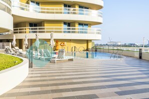 A modern hotel with a rooftop pool, lounge chairs, and a view of the city skyline.