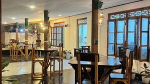 Un amplio comedor interior con mesas y sillas de madera, ventanas grandes y luces en el techo.