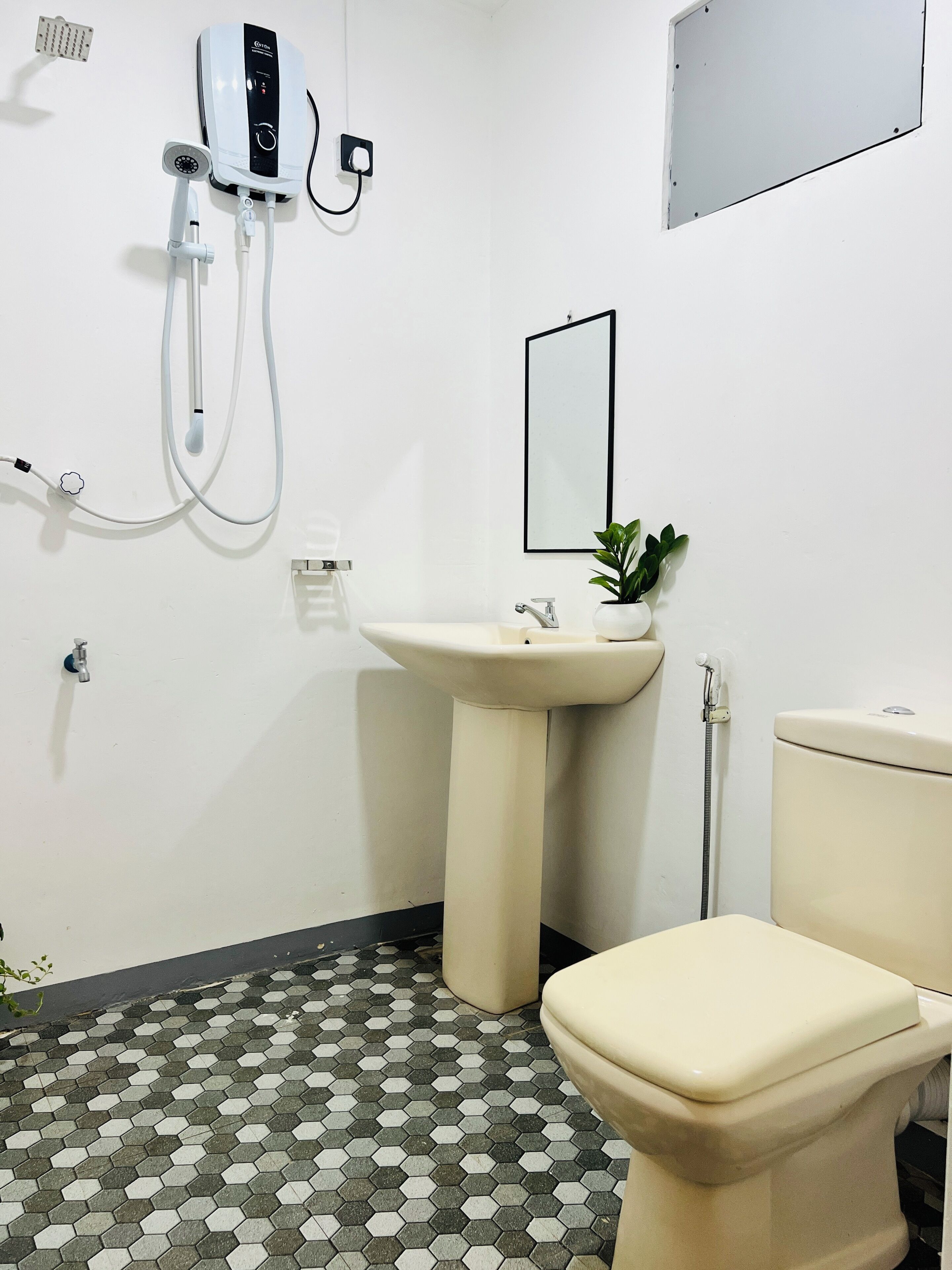 A bathroom with a hexagonal tile floor, a pedestal sink, a toilet, a handheld showerhead, and a wall-mounted mirror.