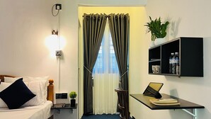 Habitación de hotel con cama, escritorio, silla y un pequeño estante con una planta y botellas de agua.