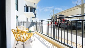 Un balcon avec des chaises jaunes, un immeuble blanc et une vue sur une rue où circulent des voitures.