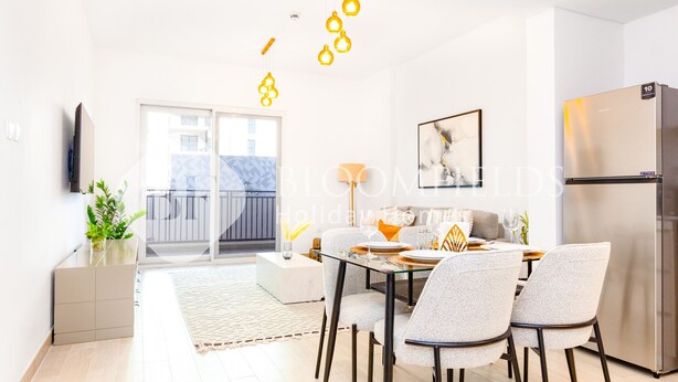 Ett modernt kök med ett kylskåp i rostfritt stål, en matplats med ett glasbord och stolar samt en balkong med utsikt.
