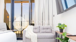 A modern living room with a grey sofa, a white throw blanket, a potted plant, and a mounted TV. - Bloomfields STU In Al Maryah Island Escape (Abu Dabi)