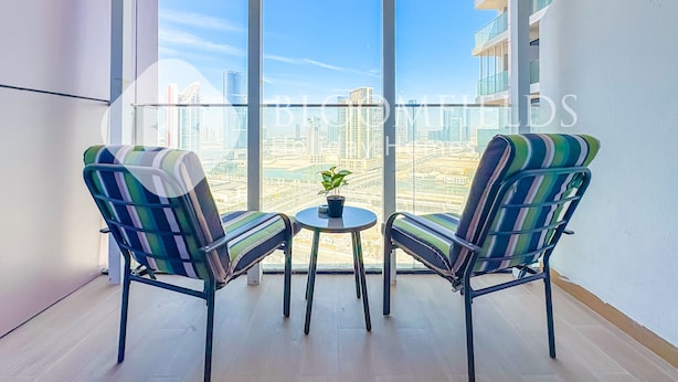 Un balcon avec deux chaises à rayures et une petite table, donnant sur un paysage urbain avec des bâtiments modernes.