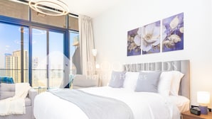 Une chambre d’hôtel moderne dotée d’un grand lit, d’un canapé et offrant une vue sur la ville grâce à de grandes fenêtres du sol au plafond.