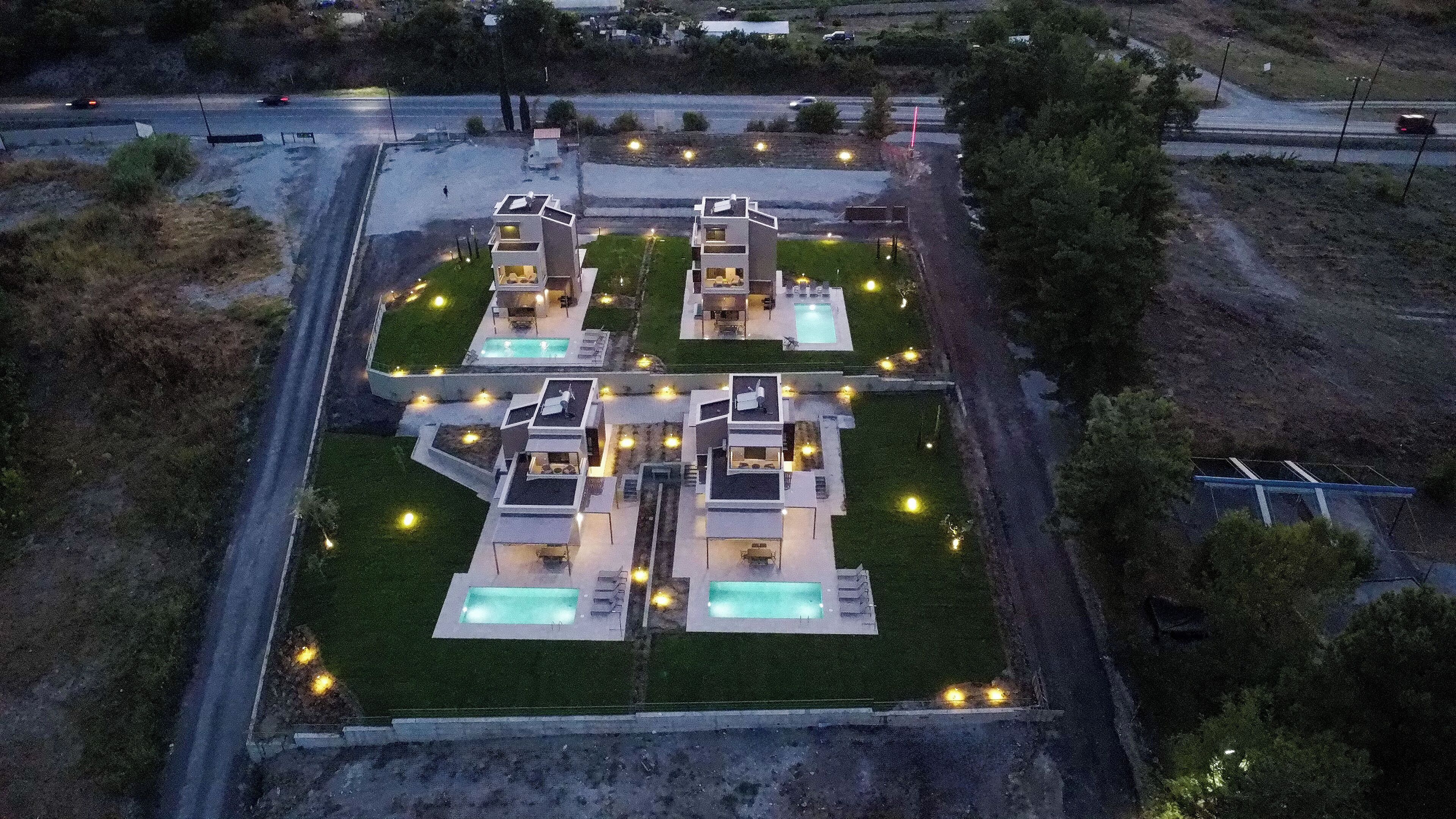 Un complexe résidentiel moderne comprenant plusieurs maisons, chacune dotée d’une piscine et d’un éclairage extérieur.