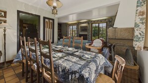 A dining area with a table set for four, wooden chairs, a hanging light fixture, and a view of the garden through the window. - House for 10 with large garden, 250m from the sea (Louannec)