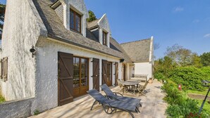 A stone house with a patio, a table, and two chairs. - House for 10 with large garden, 250m from the sea (Louannec)