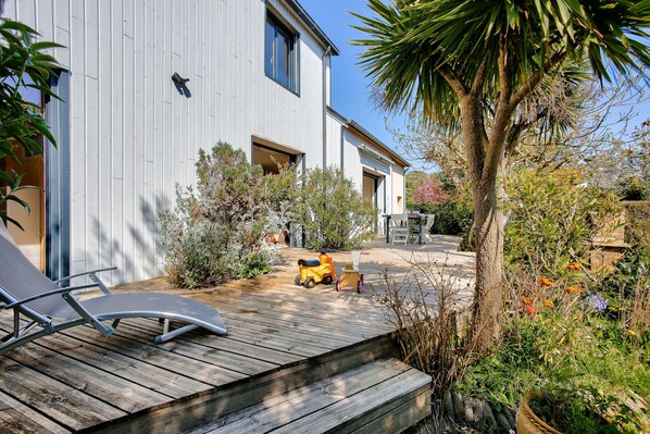 A modern house with a wooden deck, a small garden, and a palm tree.