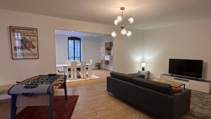 A modern living room with a foosball table, a sofa, a TV, and a dining area with a window. - Modern city-center gîte in Moulins for 4 with Wifi (Moulins)