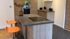A modern kitchen with a central island, two orange bar stools, a built-in oven, and a coffee machine. - Modern city-center gîte in Moulins for 4 with Wifi (Moulins)