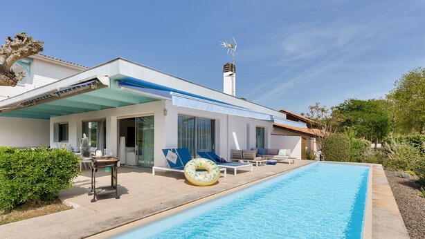 Une maison moderne dotée d’une piscine, d’un espace salon ext érieur et offrant une vue sur un ciel dégagé.