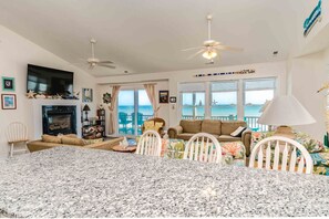 A spacious living room with a fireplace, a dining area, and a view of the ocean. - The Sugar Shak - 4 BR Oceanfront Home with Covered Porch (Surf City)